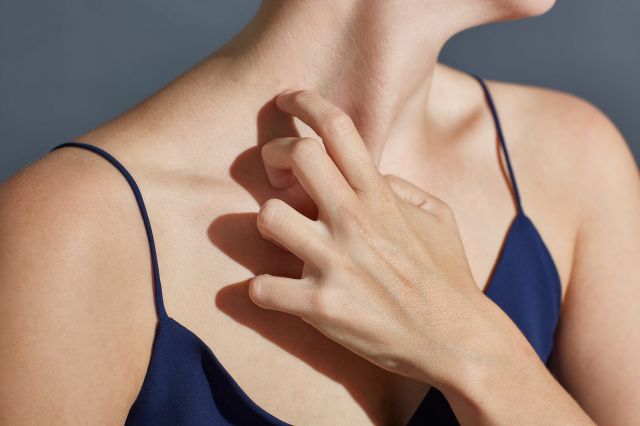 かゆみを感じて肌をかく女性